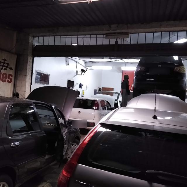Oficina com carros em atendimento e veículo no elevador